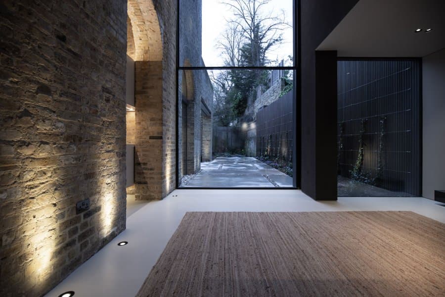 Floor-recessed uplighters grazing original brickwork, with lit courtyard beyond, at Station House